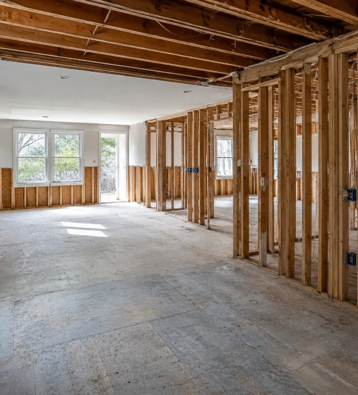 Partially gutted Maine or New Hampshire home interior with exposed framing, unfinished ceiling sections, and visible subfloor ready for reconstruction.