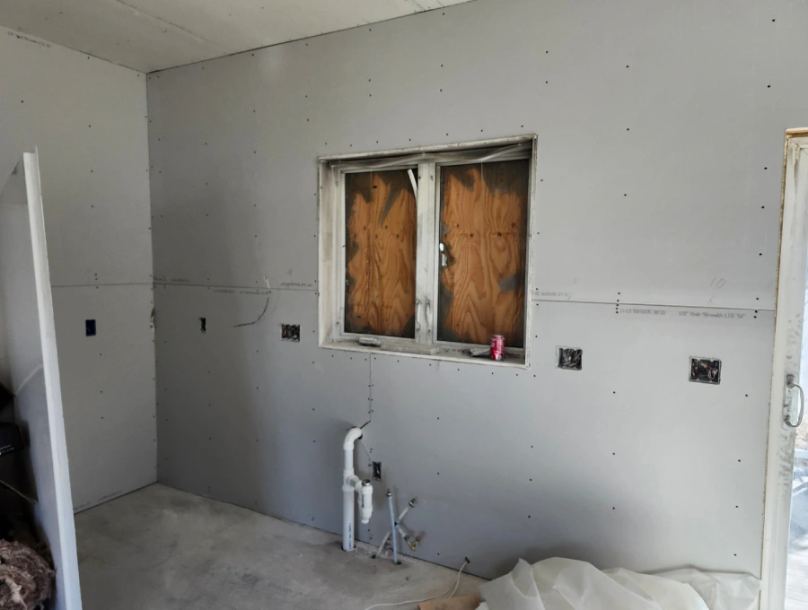 Kitchen reconstruction in progress with new drywall and sink utility preparation