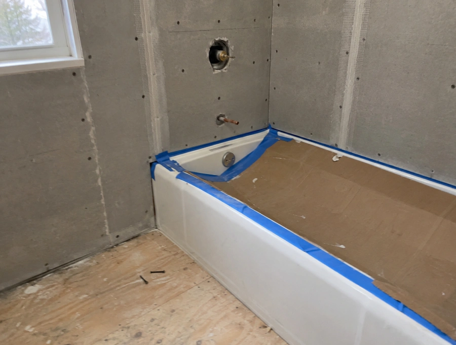 Bathroom being rebuilt after water damage, with cement backer board installed and the new tub protected with cardboard